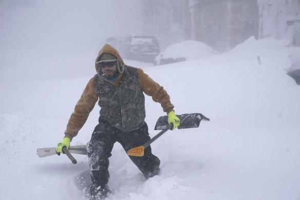 Travis Sanchez trudges over a snowdrift with a pair of shovels for a stranded motorist on Chenango Street in Buffalo, NY. 