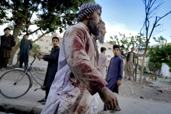 An Afghan blood-stained worshiper walks around the mosque where the explosion took place, in Kabul.