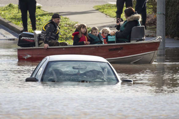 A woman and children who were stranded by high water due to flooding are rescued by a volunteer operating a boat as another person’s car is submerged near them in Abbotsford, British Columbia.