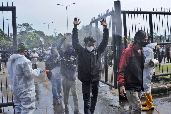 Soldiers in protective suits spray disinfectant on people entering a stadium in Bandung, West Java to receive the Sinovac vaccine.