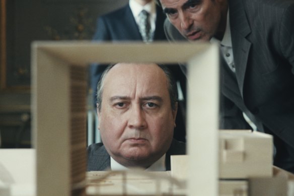 President Mitterand (Michel Fau) peers through a model of the building designed by Danish architect Johan Otto van Spreckelsen (Claes Bang) in The Great Arch.