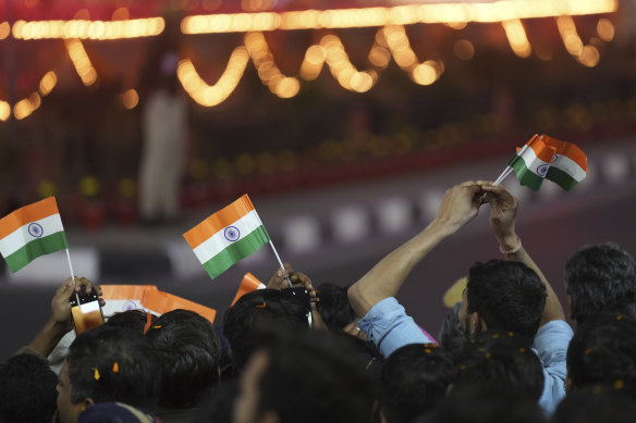 People wave the Indian national flags as they watch French President Emmanuel Macron and Indian Prime Minister Narendra Modi, unseen, drive past.