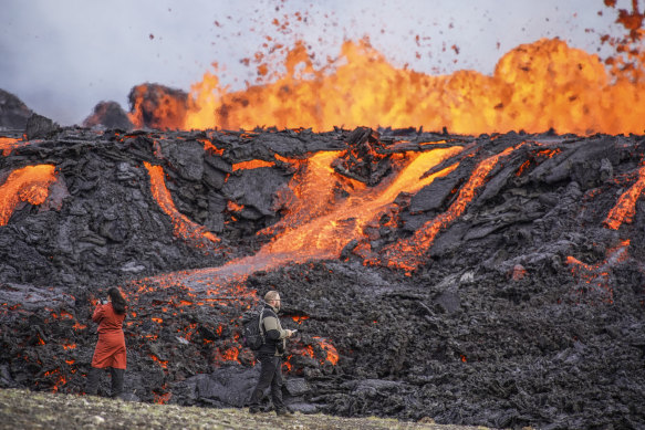 People look at the lava flowing on Fagradalsfjall volcano in Iceland. 