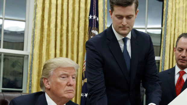 White House Staff Secretary Rob Porter, centre, hands President Donald Trump a confirmation order.