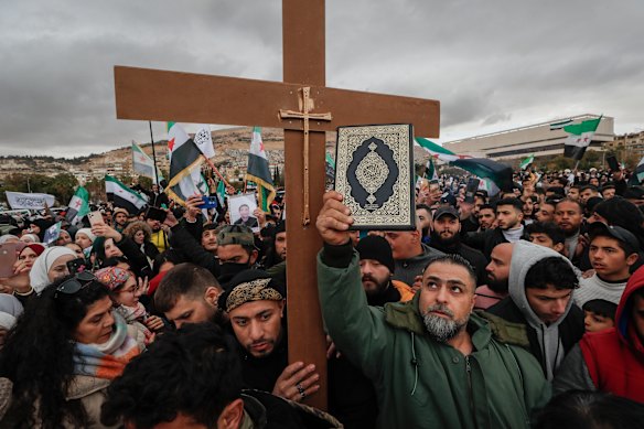 Syrians hold a copy of the Quran next to a Christian cross during a demonstration in support of unity among minorities and the ousting of the Bashar Assad government in Umayyad Square, in Damascus.