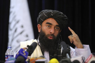 In front of a Taliban flag, Zabihullah Mujahid speaks at his first news conference.