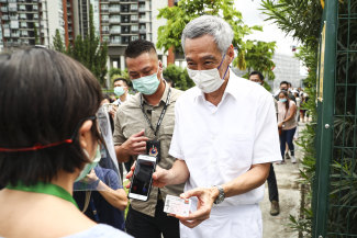 Singapore Prime Minister Lee Hsien Loong wearing a mask, which is mandatory in the island nation, shows his ID before voting last year.