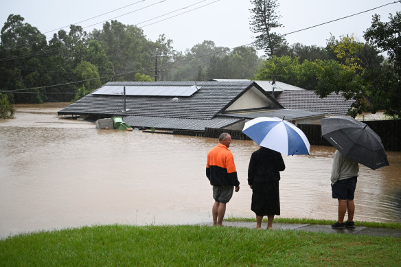 People look on as a house is inundated by floodwater in Goodna, west of Brisbane, on February 27, 2022.