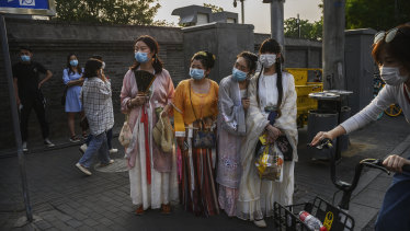 Chinese women wear traditional clothing and protective masks as they wait to cross a road in a tourist area during the May holiday in Beijing.