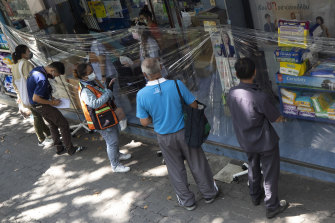 Giovedì i clienti ordinano i medicinali attraverso un foglio di plastica protettivo in una farmacia a Bangkok.