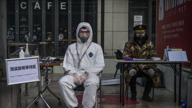 A guard waits to check temperatures and register people entering a building in Beijing. China has put huge effort into containing COVID-19.