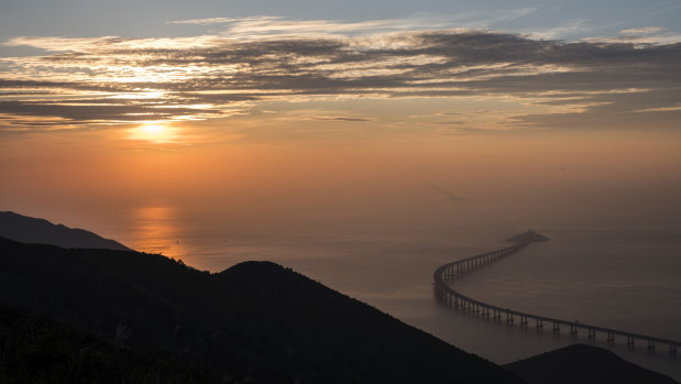 The eastern artificial island and the Hong Kong Link Road section of the Hong Kong-Zhuhai-Macau Bridge stand offshore at sunset in Hong Kong, China.