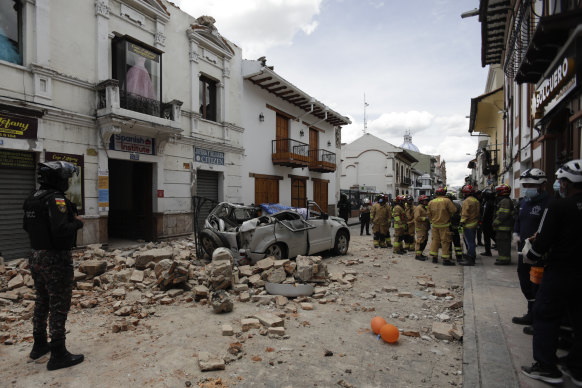 Rescue workers stand next to a car crushed by debris after an earthquake in Cuenca, Ecuador, on Saturday.