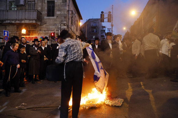 An ultra-orthodox jew burns an Israeli flag as anti-government amid protests against their military service exemptions.