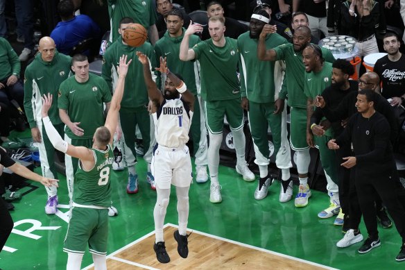 Dallas guard Kyrie Irving shoots for a three-pointer under intense scrutiny from the Celtics bench.