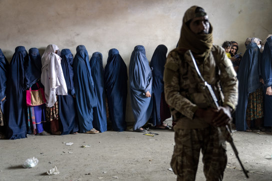 A Taliban fighter and women lined up for food rations in Kabul in 2023.