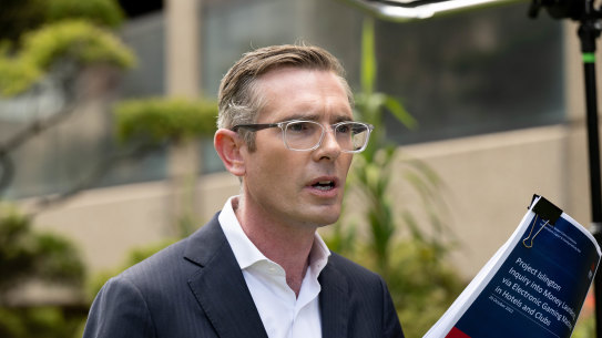 NSW Premier Dominic Perrottet on Wednesday brandishes the NSW Crime Commission report which recommended statewide cashless gaming to combat money laundering.