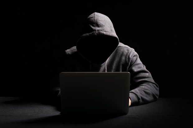 Hacker working on laptop in the dark - scam - shadowy figure online