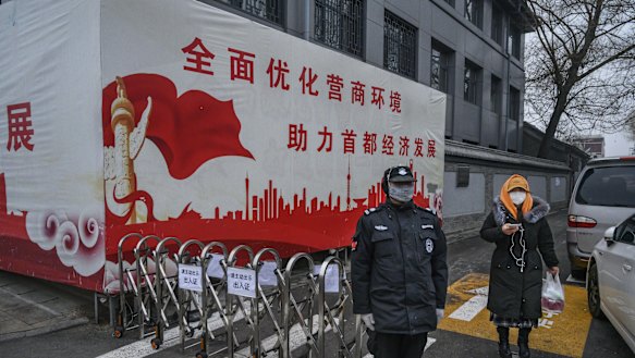 A Chinese security guard wears a protective mask as he stands at a barricade to control the entry and exit from a residential area in Beijing.