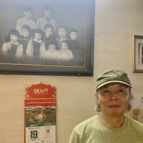 Nguyen Van Dao with his family’s treasured portrait at Cafe Giang. He is pictured as an infant, bottom row, second from left.