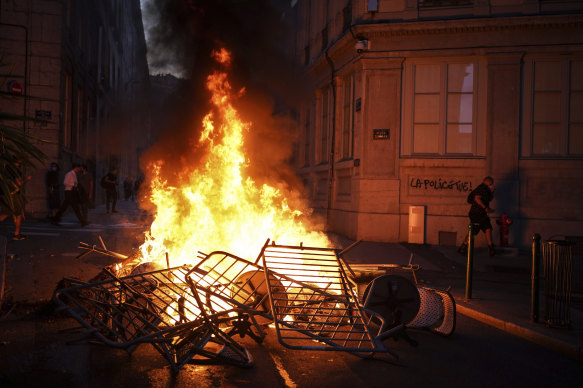 A man passes by a wall illuminated by a burning barricade on which is written “Police kills” in the centre of Lyon, central France, on Friday.