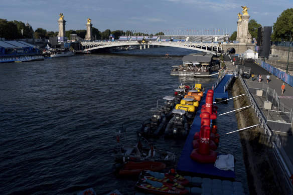 Watercraft and buoys sit along the Seine river as the triathlon event venue on the Pont Alexandre III bridge stands in the background at the 2024 Summer Olympics, Sunday, July 28, 2024, in Paris. (AP Photo/David Goldman)