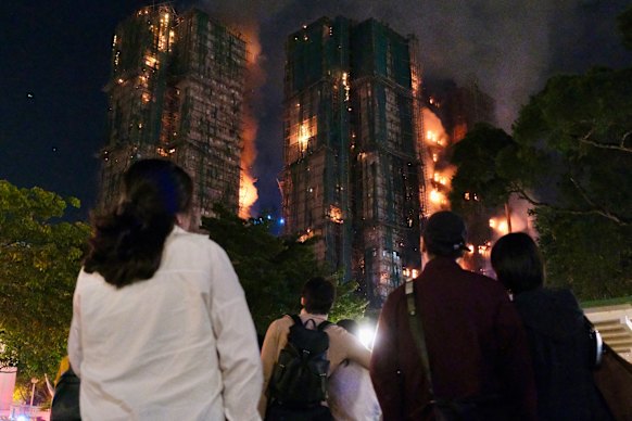 People look on as thick smoke and flames rise from the Wang Fuk Court apartment complex, home to about 5000 people in Hong Kong.