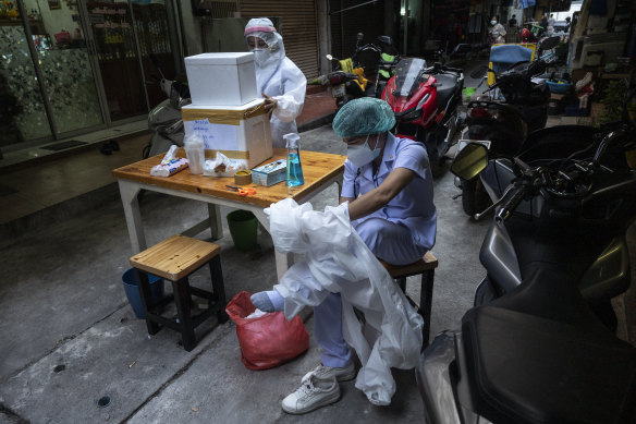 A health worker in Bangkok takes off the PPE gear, while her colleague seals the foam box containing swab samples.