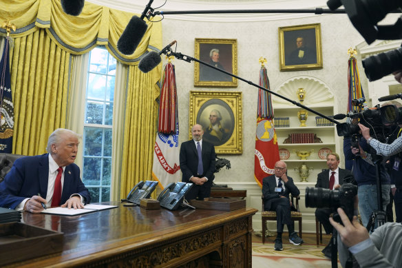 President Donald Trump signs an executive order as commerce secretary nominee Howard Lutnick (standing) and billionaires Rupert Murdoch and Larry Ellison sit in the Oval Office.