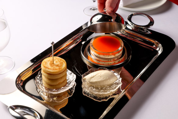 A mirrored tray of potted spanner crab set under sunset-hued shellfish butter served with a stack of pikelets and a quenelle of creme fraiche. 