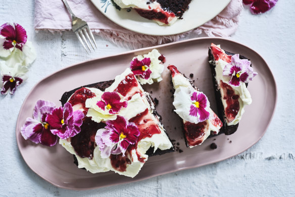 Chocolate loaf cake topped with mascarpone icing, red jam and flowers.