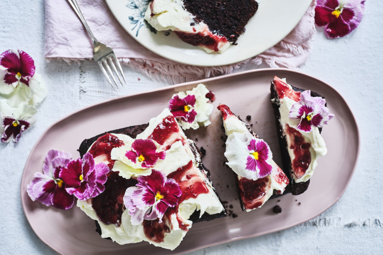 Chocolate loaf cake topped with mascarpone icing, red jam and flowers.