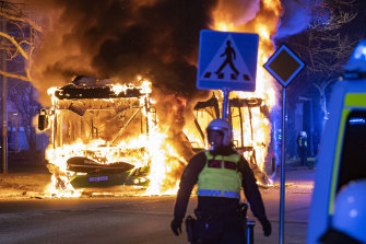 Çevik kuvvet polisi hafta sonu Malmö'de bir sokakta bir belediye otobüsünün yandığını izliyor.