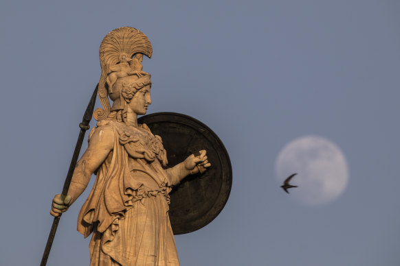 The flower moon rises behind the statue of the ancient Greek goddess of wisdom, Athena, atop the Academy of Athens building.