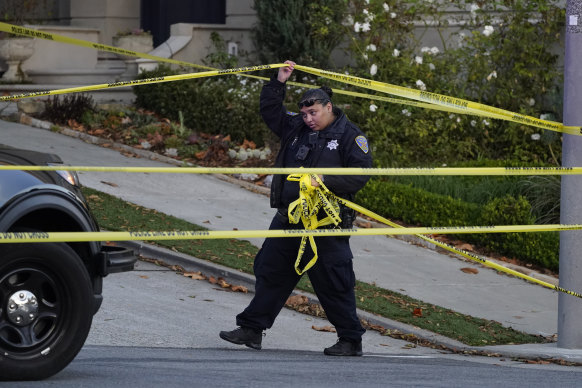 A police officer rolls out more yellow tape on the closed street near the Pelosis’ home.