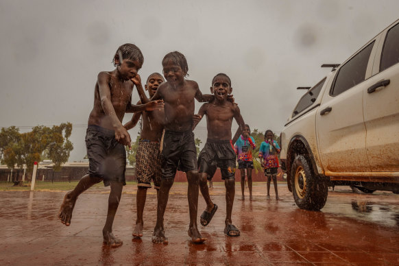 A group of children dances barefoot as the rain falls.