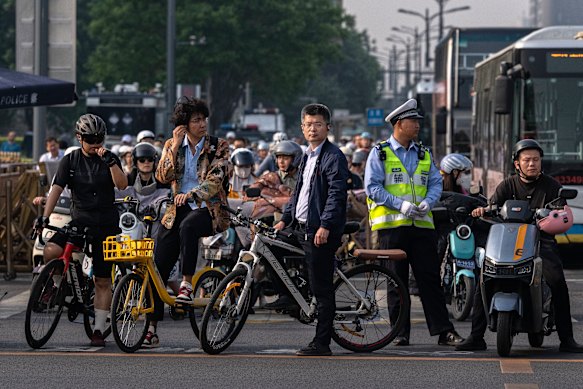 Os passageiros esperam num semáforo ao lado de um policial perto da Praça Tiananmen, enquanto a cidade se prepara para receber o presidente dos EUA.