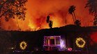 A helicopter drops water on the Palisades Fire behind a home with Christmas lights in Mandeville Canyon, Friday, Jan. 10, 2025, in Los Angeles. (AP Photo/Ethan Swope)