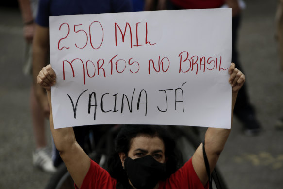 A demonstrator holds a sign written in Portuguese that reads “250 thousand dead in Brazil, Vaccine Now.”