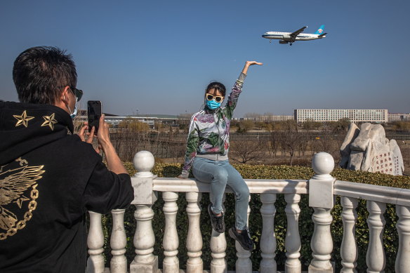 A woman wearing a protective face mask poses for photos as a plane lands at the Capital International Airport in Beijing. Chinese students and expatriates were discouraged from returning home during the pandemic.