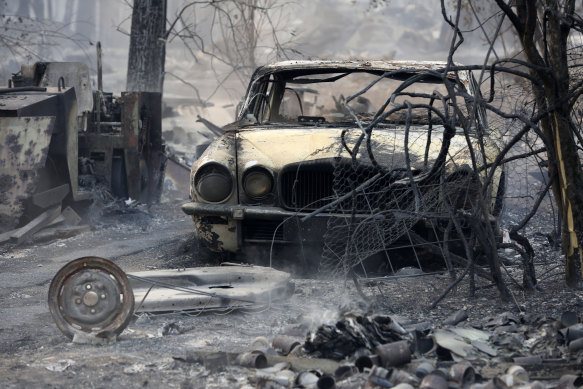 The burnt out shell of a Jaguar vehicle sits in the ruins of a smouldering house on Old Bar road near Taree on Saturday.