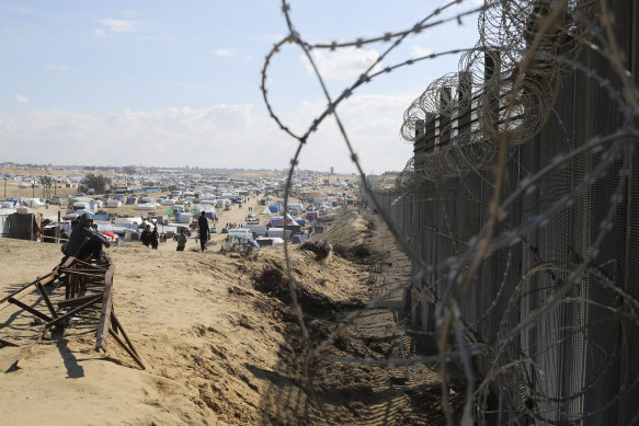 Palestinians displaced by the Israeli air and ground attack on the Gaza Strip sit next to the border fence with Egypt in Rafah.