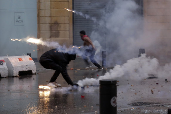 Protesters attempt to throw tear-gas canisters back at riot police.