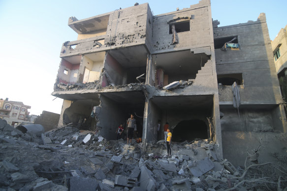 Palestinians stand by a building destroyed in an Israeli airstrike in the Rafah border, Gaza Strip.