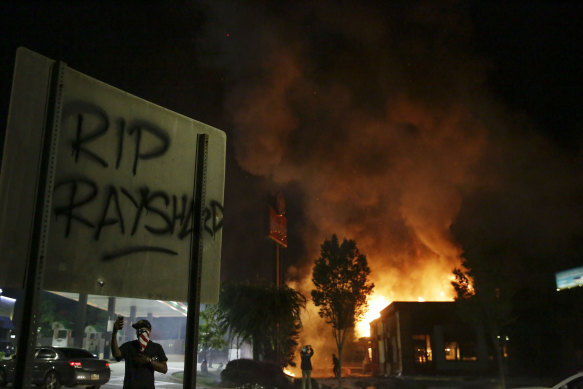 'RIP Rayshard' is spray painted on a sign as flames engulf the Wendy's restaurant during protests on Saturday, June 13.