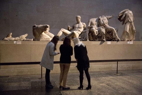 Women stand by a marble statue of a naked youth thought to represent Greek god Dionysos (centre) from the east pediment of the Parthenon at the British Museum in London in 2015.