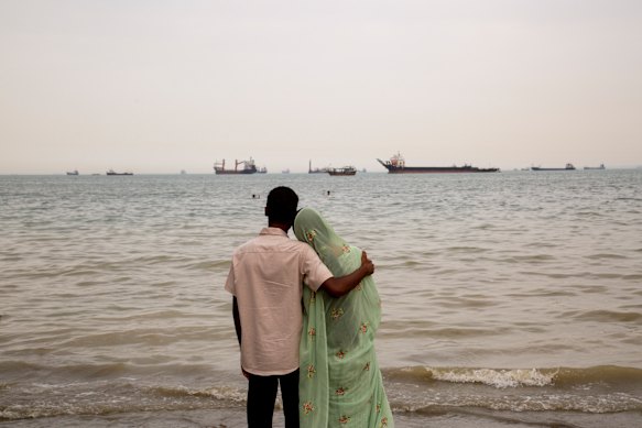 A man and woman on an Iranian beach look out at ships anchored in the Strait of Hormuz.