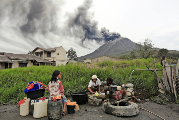 Villagers do their laundry as Mount Sinabung spews volcanic materials during an eruption, in Karo, North Sumatra, on Friday, August 14.