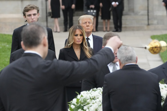 Former President Donald Trump stands behind his wife Melania as she watches a priest wave incense around the coffin of her late mother Amalija Knavs.