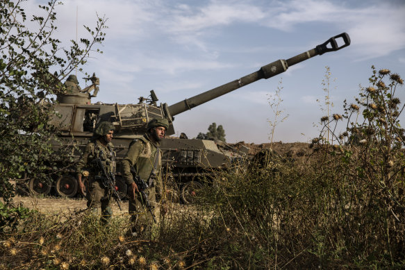 Two Israeli soldiers walk around an artillery unit, at the Israeli Gaza border, on Sunday.